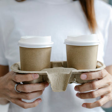 Ragazza che tiene vassoio asporto di cartoncino con due bicchieri di carta color avana con tappo bianco